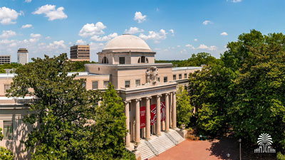 McKissick Museum on a sunny, blue-sky day with tree and gates mark.