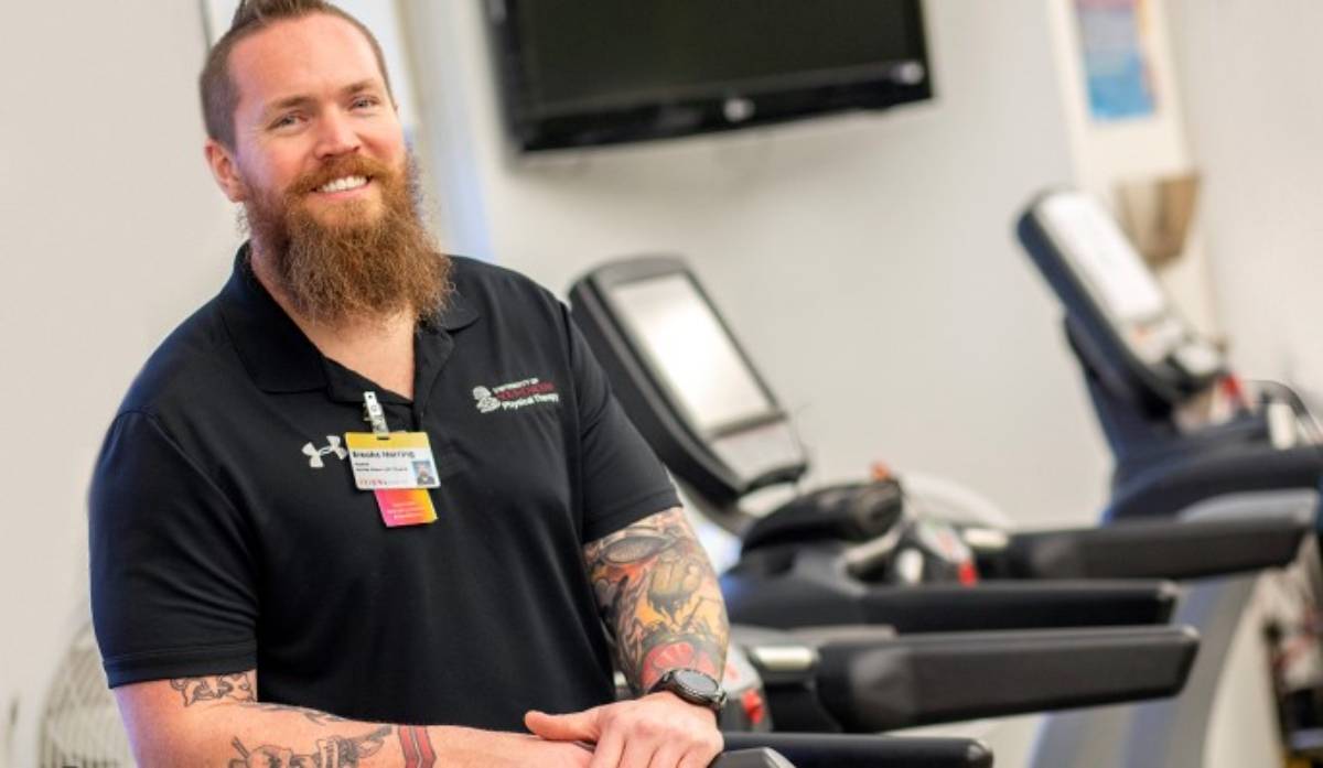 Male standing on top of a treadmill on campus smiling.