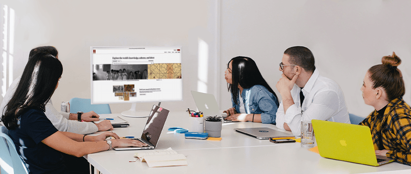 People sitting around a table and looking at a computer monitor