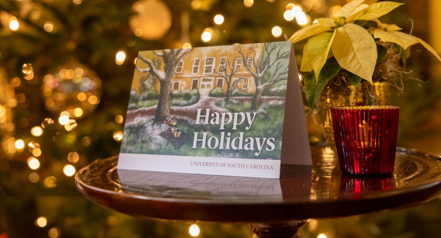 The 2024 holiday card sits on a table in the President's House next to a white poinsettia