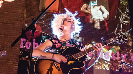 Musician on stage holding a guitar with stage lights at an evening outdoor concert. 