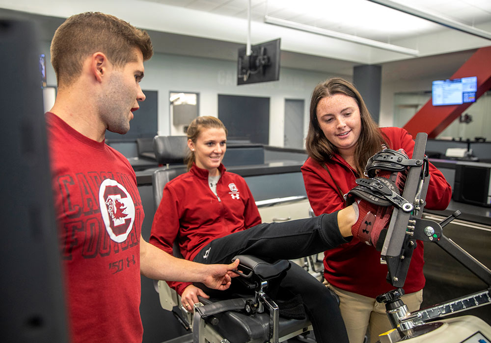 Athletic trainers with a student with her foot in device. 