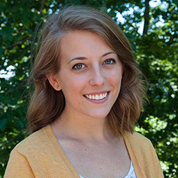 Photo of a woman with dark hair and a yellow cardigan on standing outside 