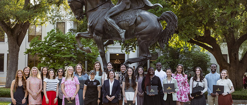 Group of student award winners and Dean Angela Baum in front of the Torchbearer statue