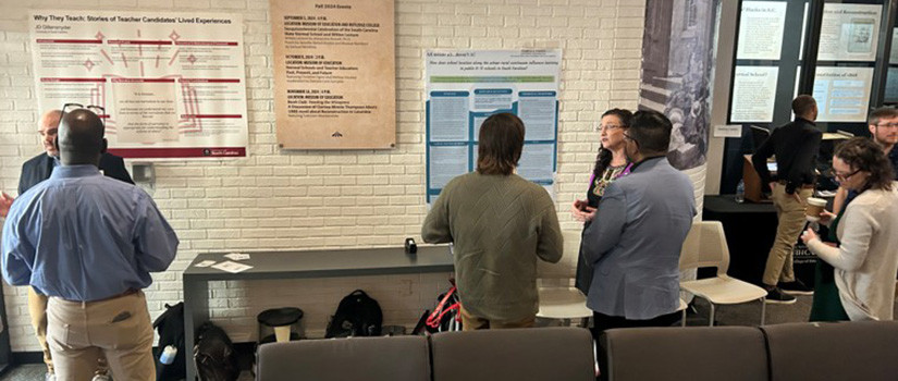 People looking at posters. A grey couch is in the foreground.