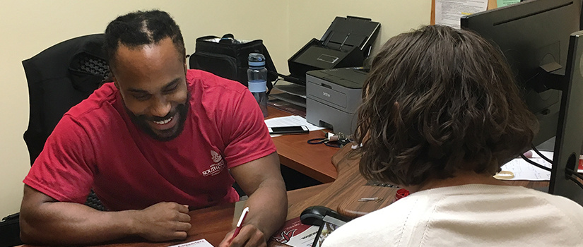 a smiling advisor leans over to write something for a student