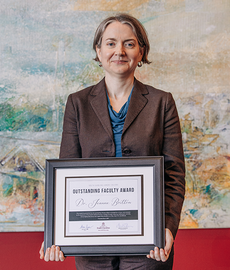 Jeanne Britton standing in the Koger Center lobby holding her 2025 SCHC outstanding faculty award