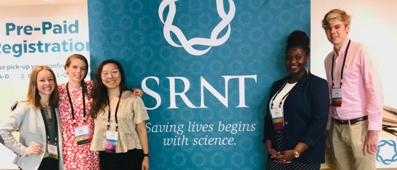 Graduate students standing in front of a banner at a conference