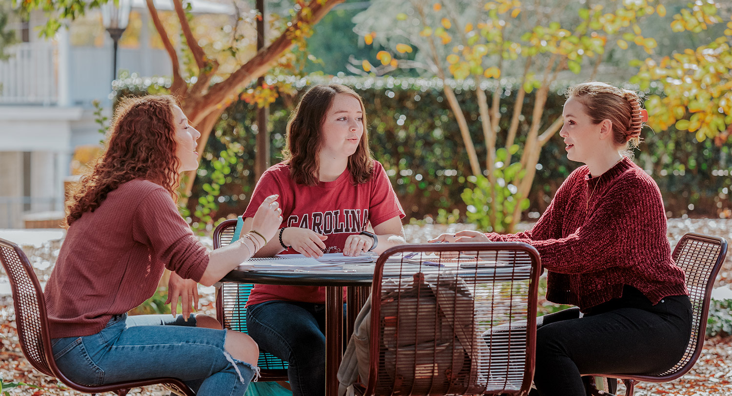 Three students study by Thomas Cooper library.