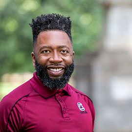 Julian Williams stands in the fore, wearing a garnet polo shirt, with the Maxcy monument out of focus in the background