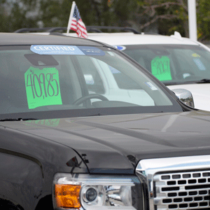 A car on a sales lot with a green price sticker on the windshield with other cars in the background.