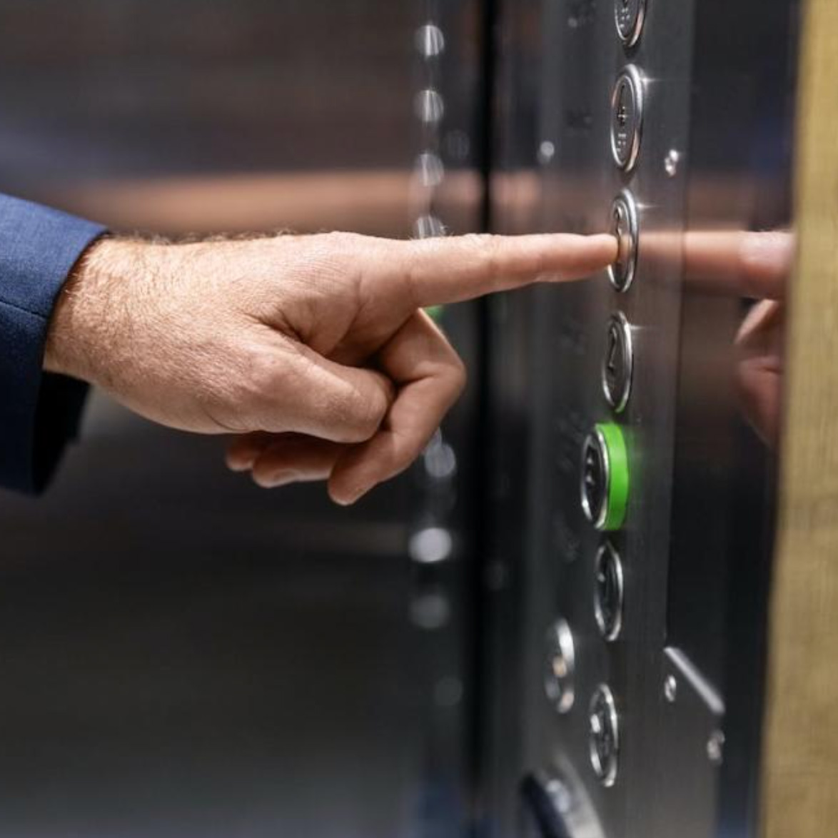 A hand presses an elevator button