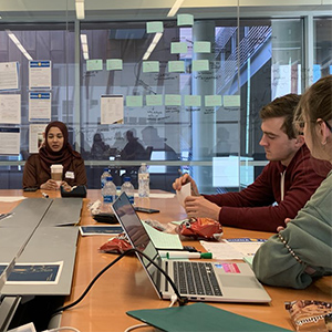 Three internatinal business students sit at table and work on laptops as part of a class