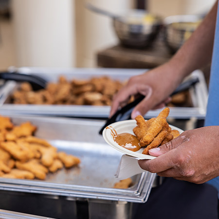 Person getting a dino chicken nugget from a buffet.