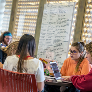 Students sit at a table, using their laptops to study. 