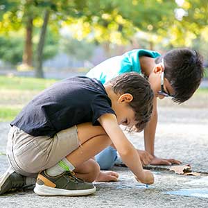 Two young boys draw with sidewalk chalk on a sunny day. 