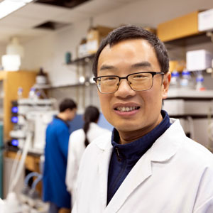 Man stands in a lab setting with equipment and people in the background