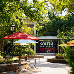 sign reading "university of south carolina" seen through a patio with trees and tables