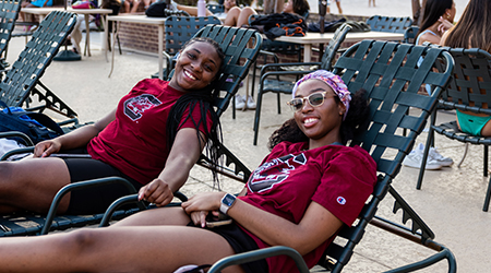 two girls in gamecock shirts laying on pool loungers