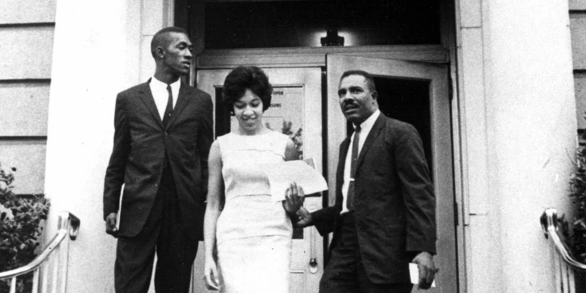 three people stand in a doorway outside a building in an archival image